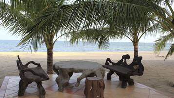 A beachside seating area with a round table and two chairs, surrounded by palm trees and a view of the sea.
