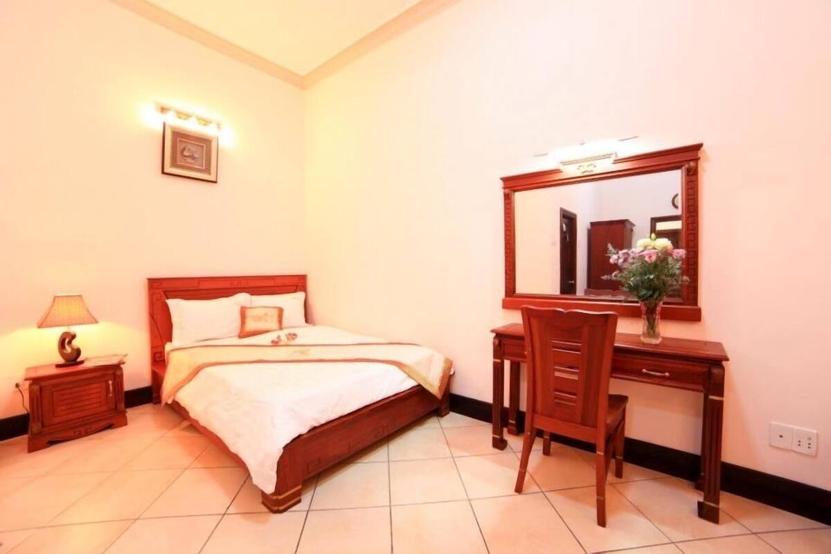 A hotel room with a bed, a desk, a chair, a lamp, and a mirror.