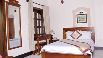 A neatly arranged bedroom with a wooden bed, a bedside table with a lamp, a mirror, and a framed picture on the wall.