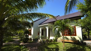 Una casa de dos pisos con techo de tejas, rodeada de exuberante vegetación y palmeras.