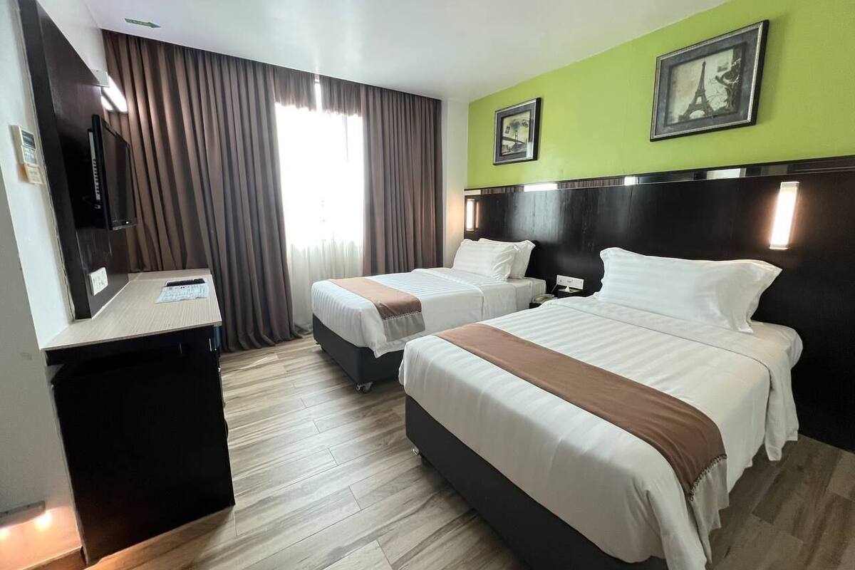 A hotel room with two beds, a desk, and a television.