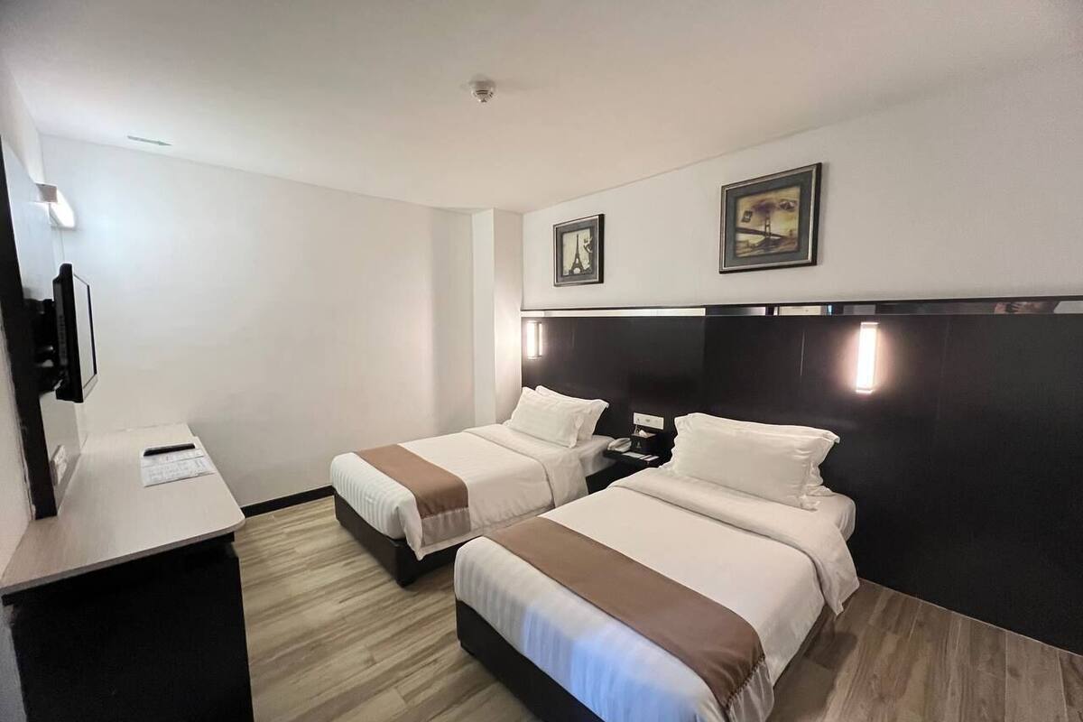 A hotel room with two beds, a desk, and a TV.