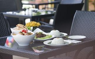 Una mesa servida con diversos platos, incluyendo arroz, verduras y carne, junto con una silla de mimbre y una mesa de vidrio.