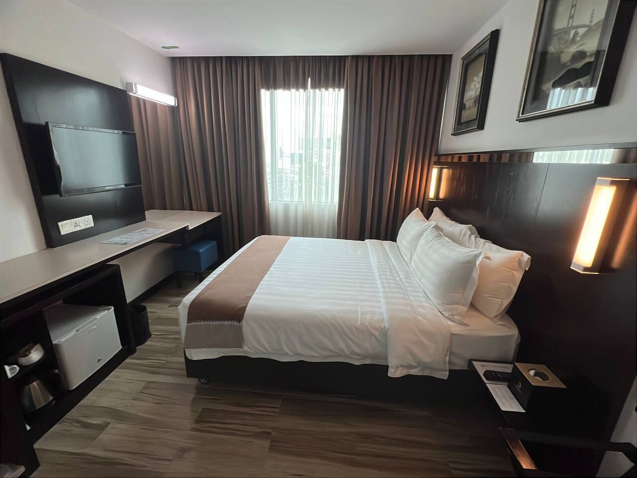 A hotel room with a bed, a desk, a TV, and a window with curtains.