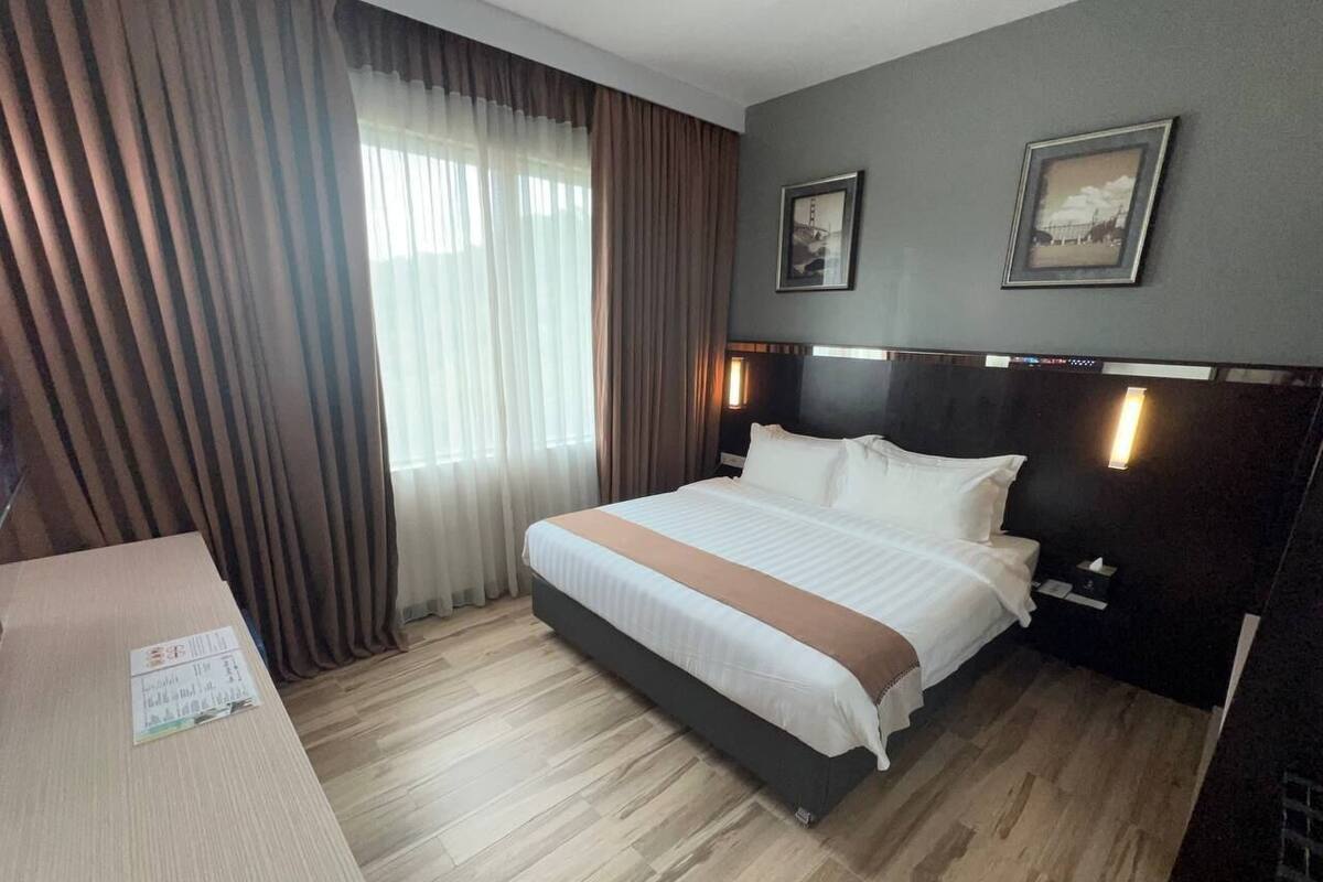 A hotel room with a bed, a bedside table, a nightstand, and a window with curtains.