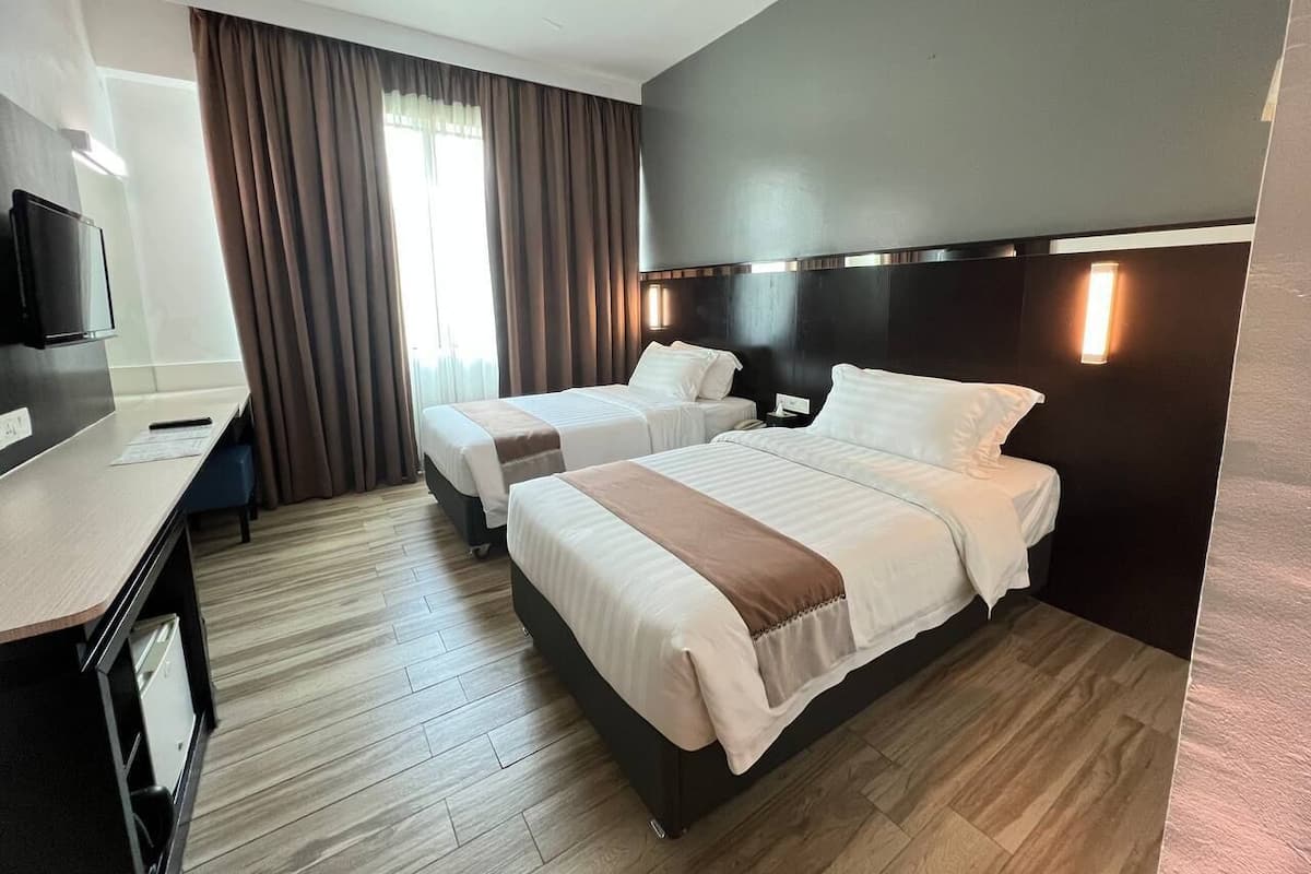 A hotel room with two beds, a desk, a TV, and a window with curtains.