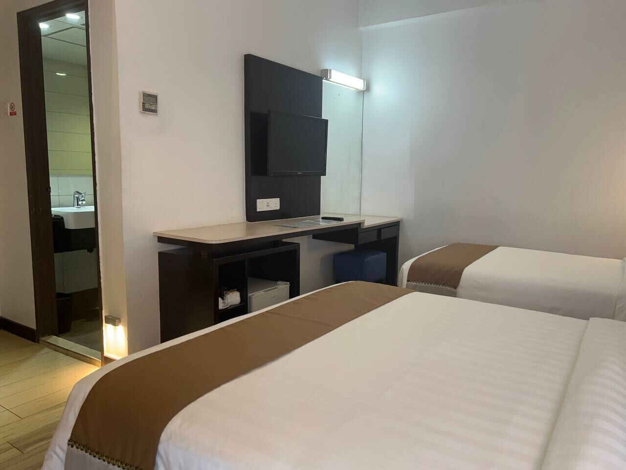 Habitación de hotel con dos camas, un escritorio, un televisor de pantalla plana y un espejo.