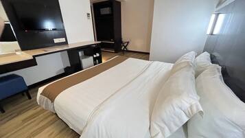 Quarto de hotel com cama, escrivaninha, cadeira e televisão.