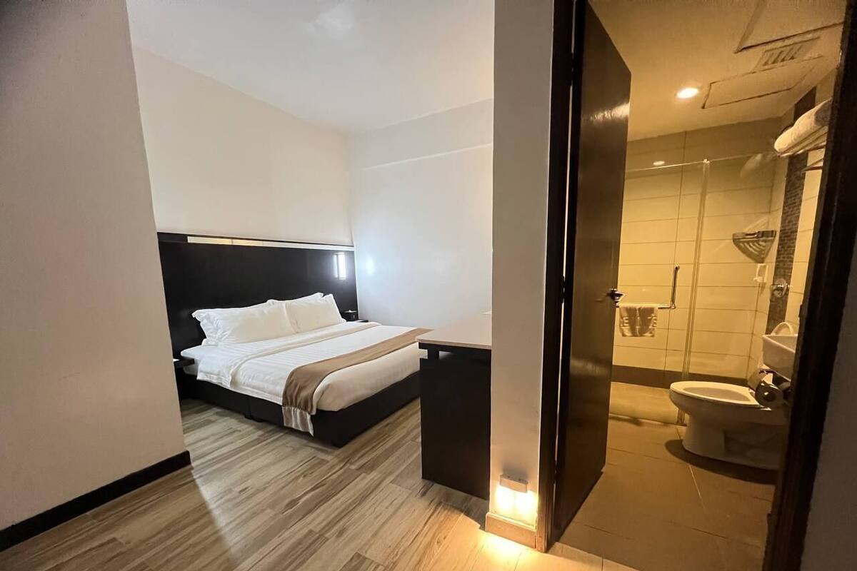 A modern hotel room with a bed, bedside table, and a view into the bathroom.