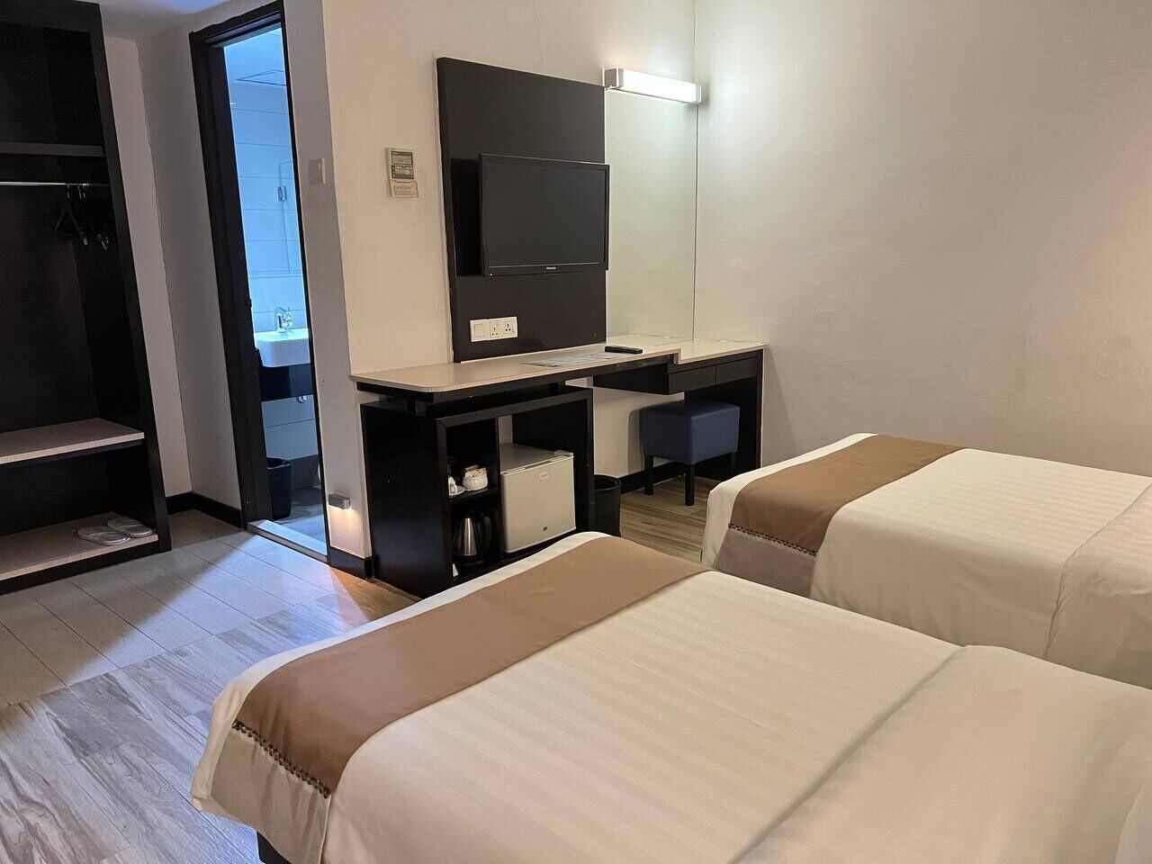 Habitación de hotel con dos camas, un escritorio, televisión de pantalla plana, kitchenette pequeña y un espejo.