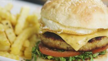 A sandwich with a sesame seed bun, lettuce, tomato, and a grilled patty, accompanied by a side of French fries.