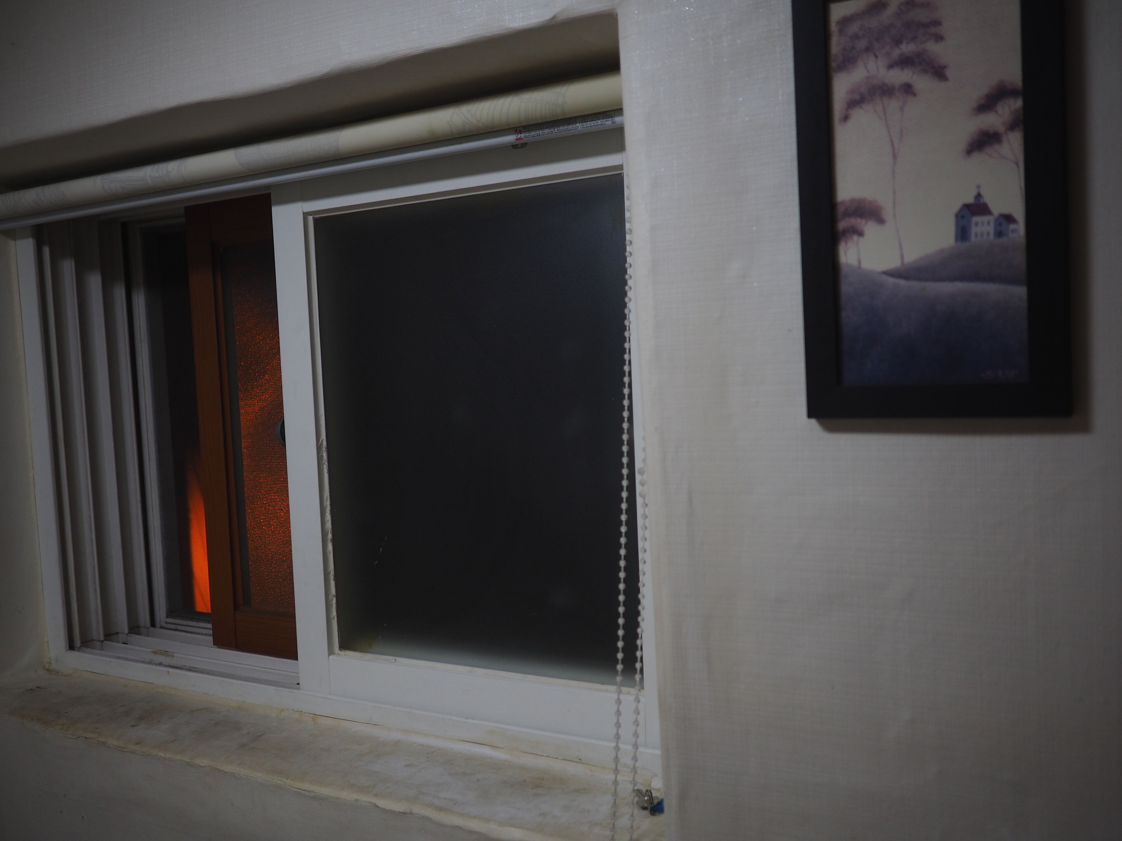 A window with a view of a landscape painting, a closed door, and a window blind.