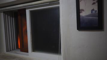 A window with a view of a landscape painting, a closed door, and a window blind.