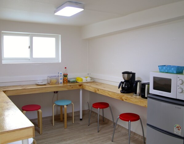 A compact kitchen with a wooden countertop, a microwave, a coffee maker, and four stools.