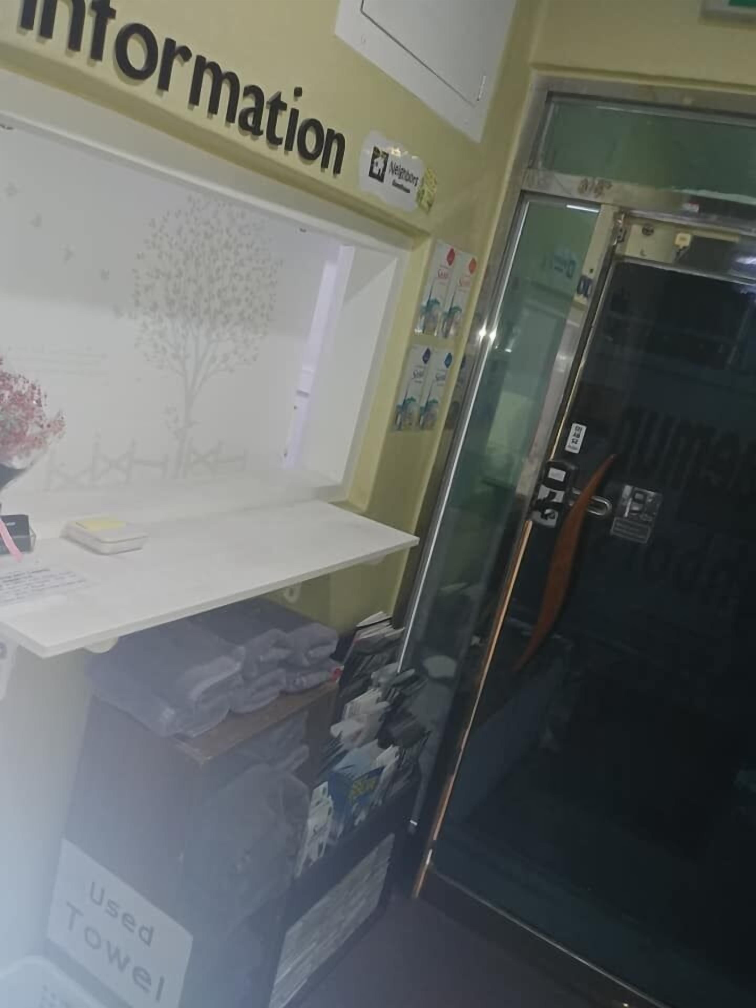 Una zona de recepción con un cartel que dice 'Information', un mostrador con un florero y un refrigerador.