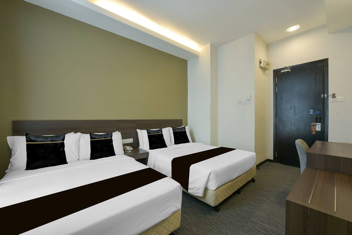 A hotel room with two beds, a desk, and a door.