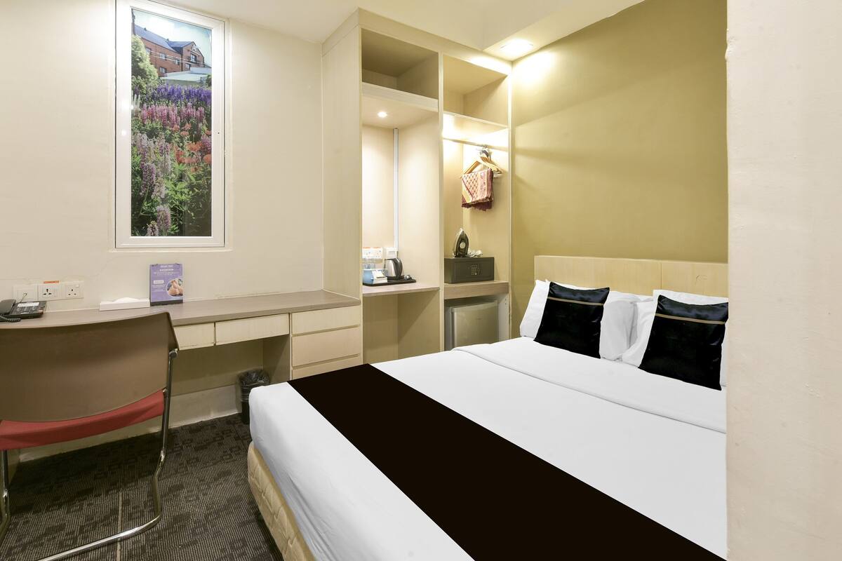 A hotel room with a bed, desk, chair, and a window with a view of flowers.