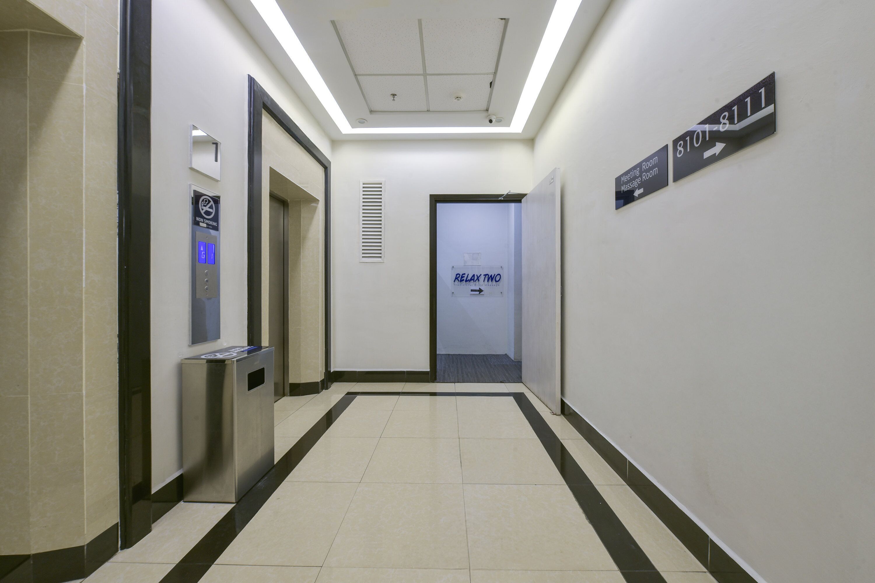 A hallway with an elevator, a sign for the meeting room, and a sign for the massage room.