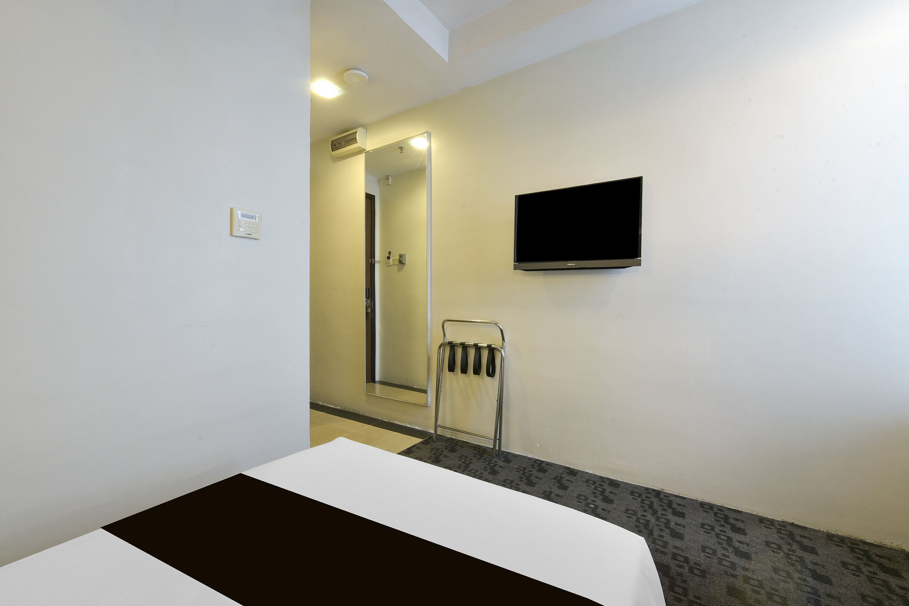 Habitación de hotel con cama, televisor montado en la pared, zona de ducha y toallero.