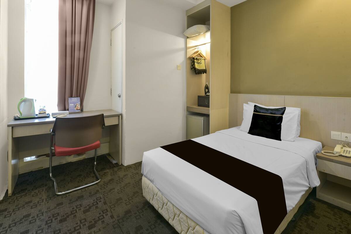 A hotel room with a bed, desk, chair, and a telephone on the nightstand.