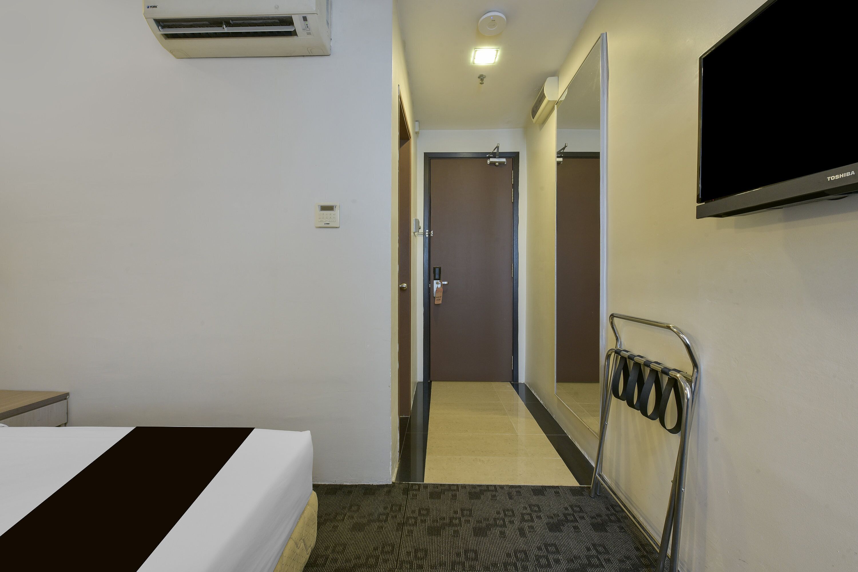 Habitación de hotel con cama, televisor, espejo y puerta que da a un baño.