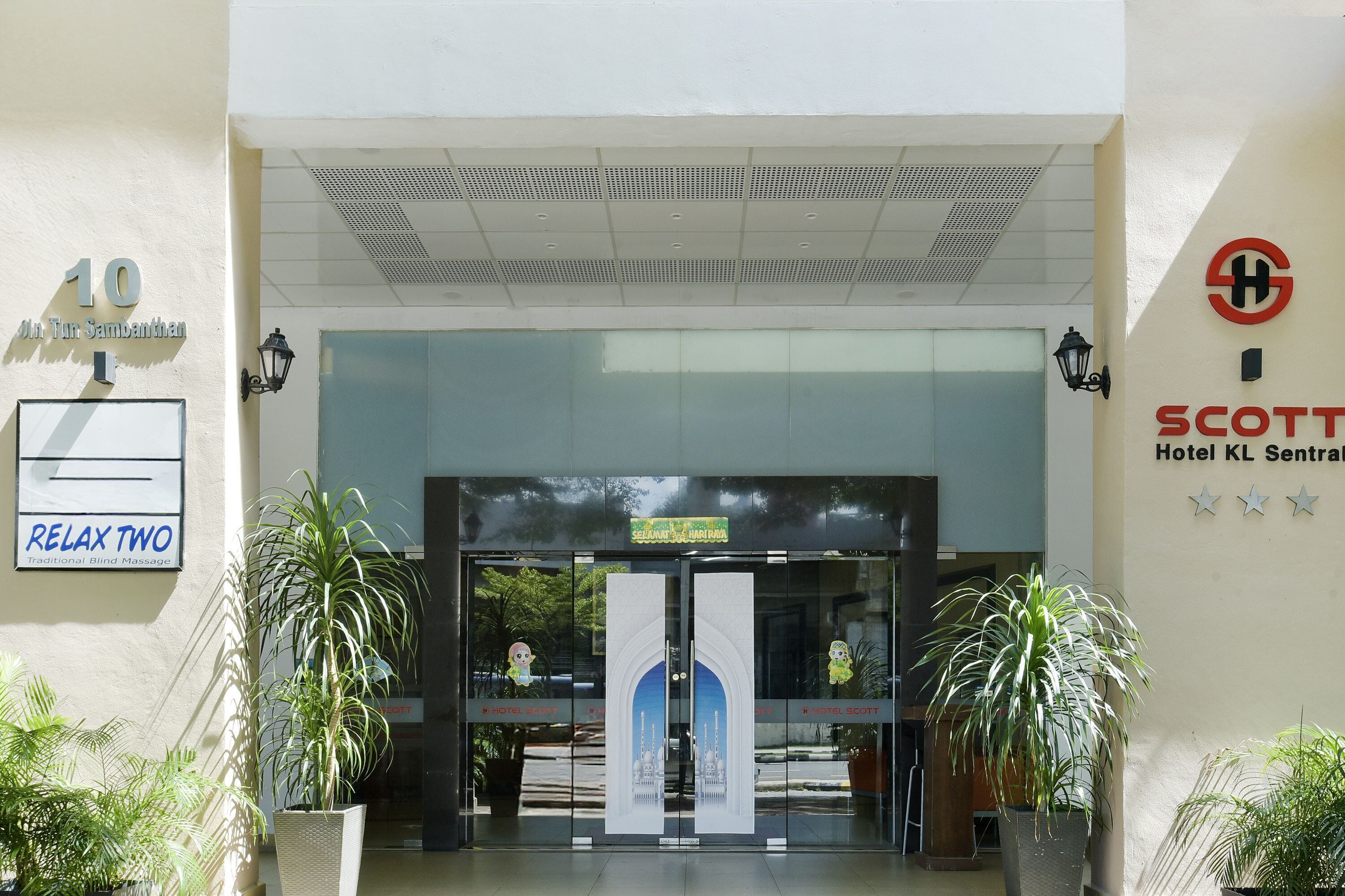 Entrada de un hotel con un letrero que dice 'Relax Two Masaje Corporal Tradicional', un letrero de 'Scott Hotel KL Sentral' y el número '10' en la pared.