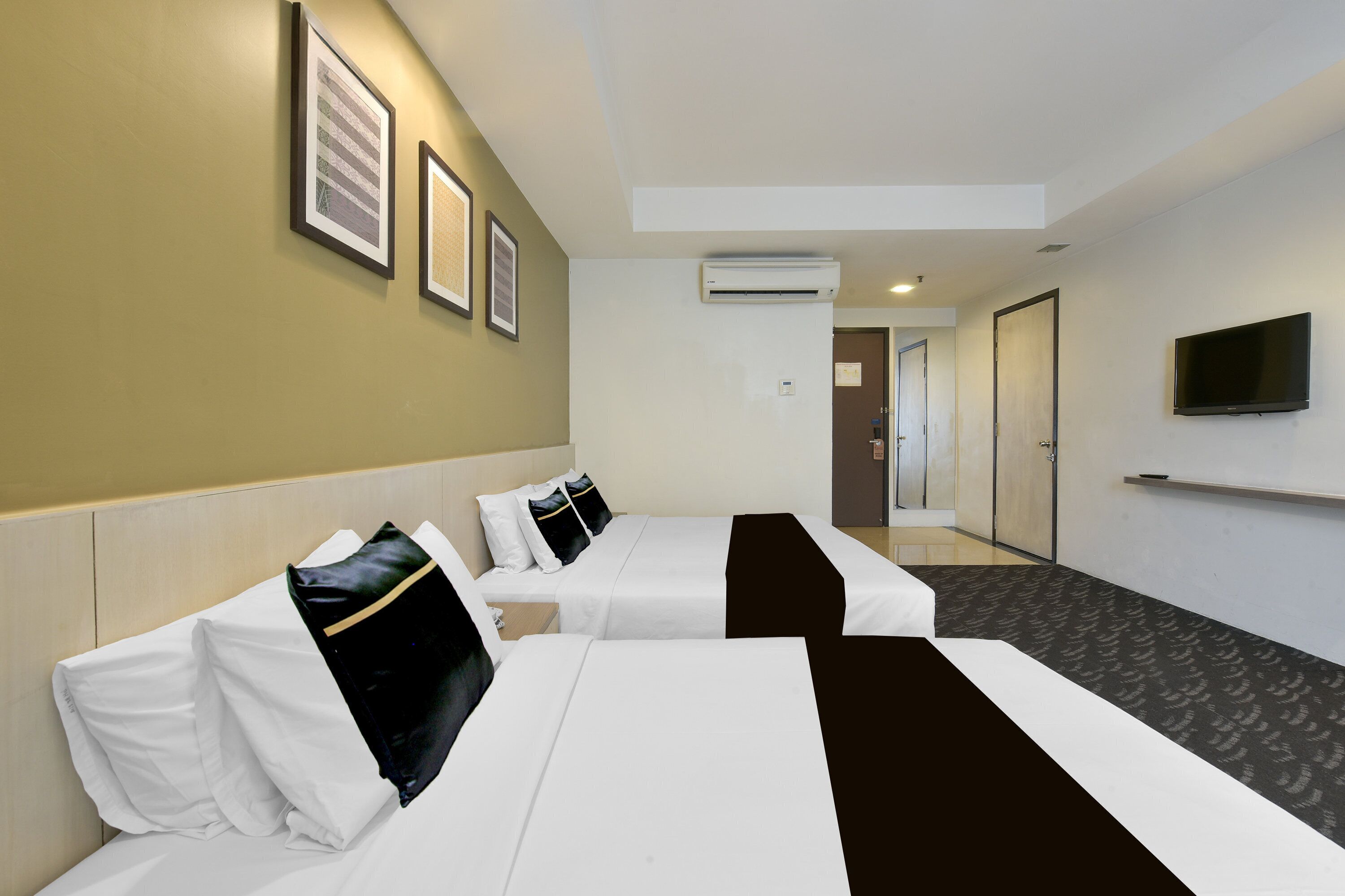 Habitación de hotel con dos camas, un televisor de pantalla plana, fotografías enmarcadas en la pared y un equipo de aire acondicionado.