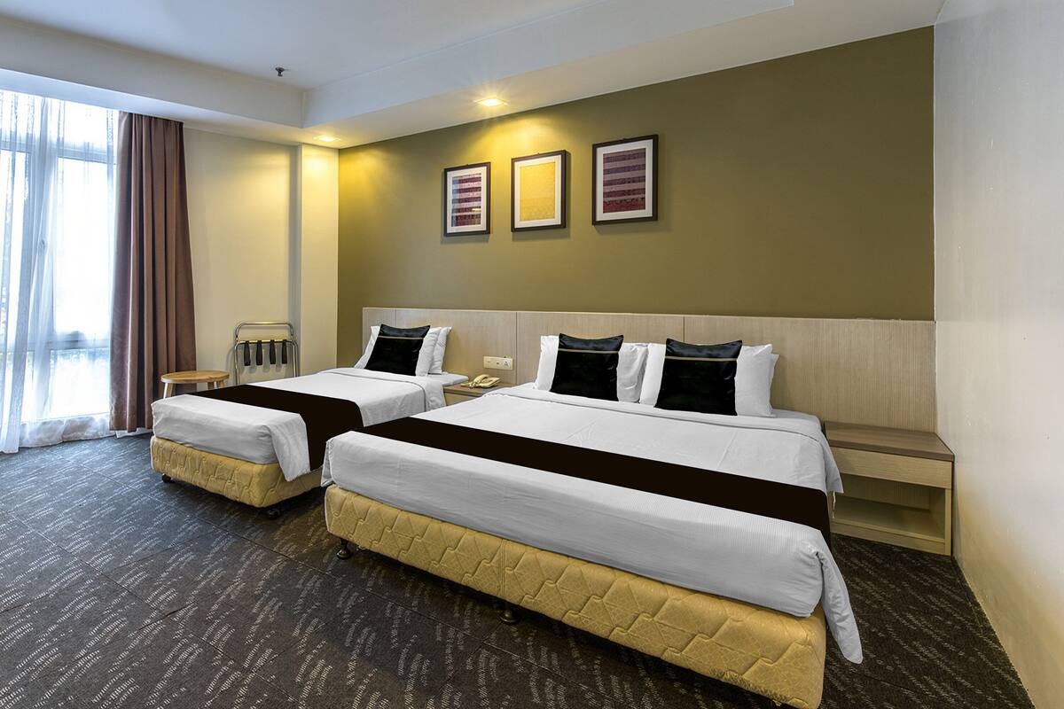 A hotel room with two beds, a bedside table, a chair, and a large window with curtains.