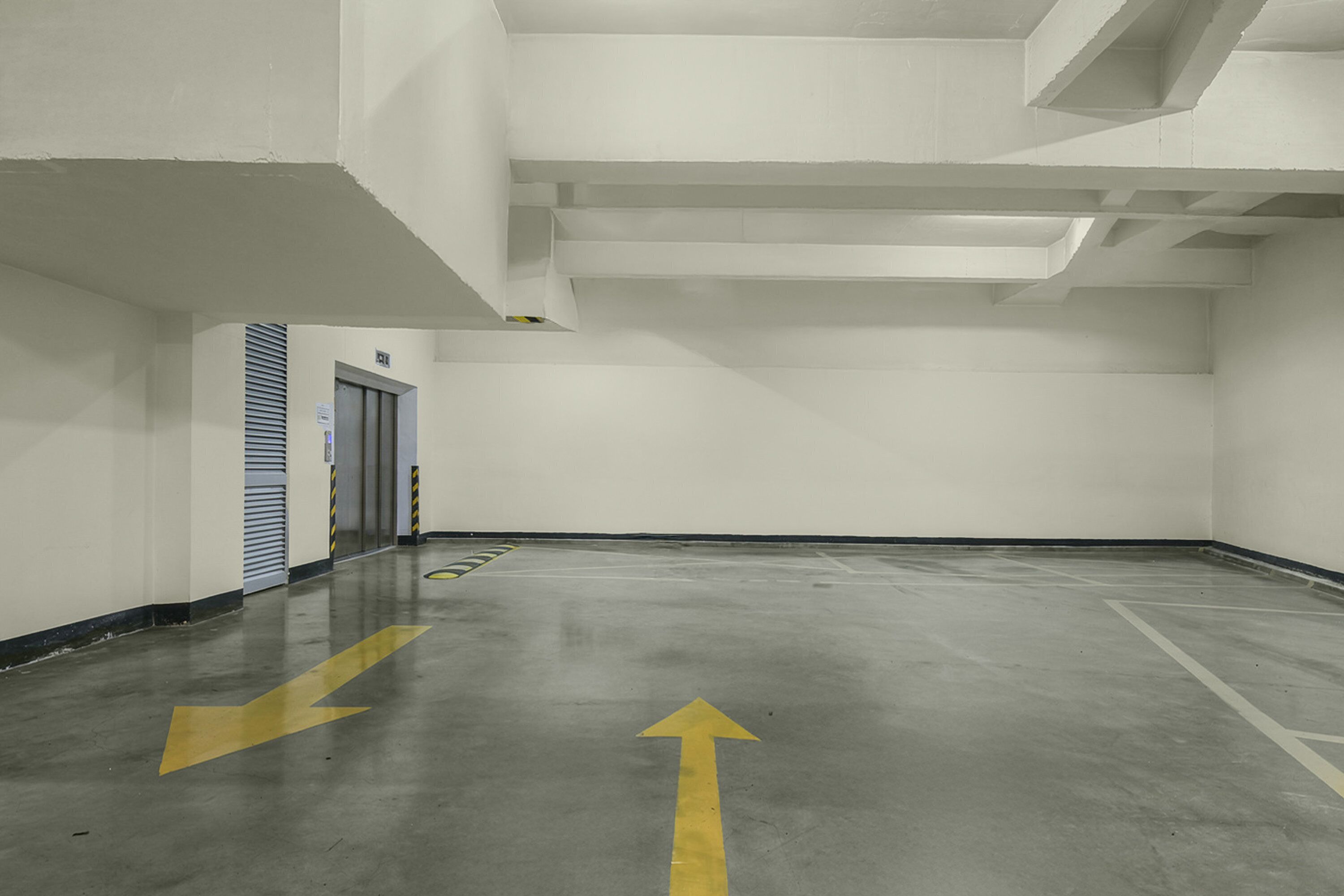 A parking garage with directional arrows on the floor, a door, and a vent on the wall.