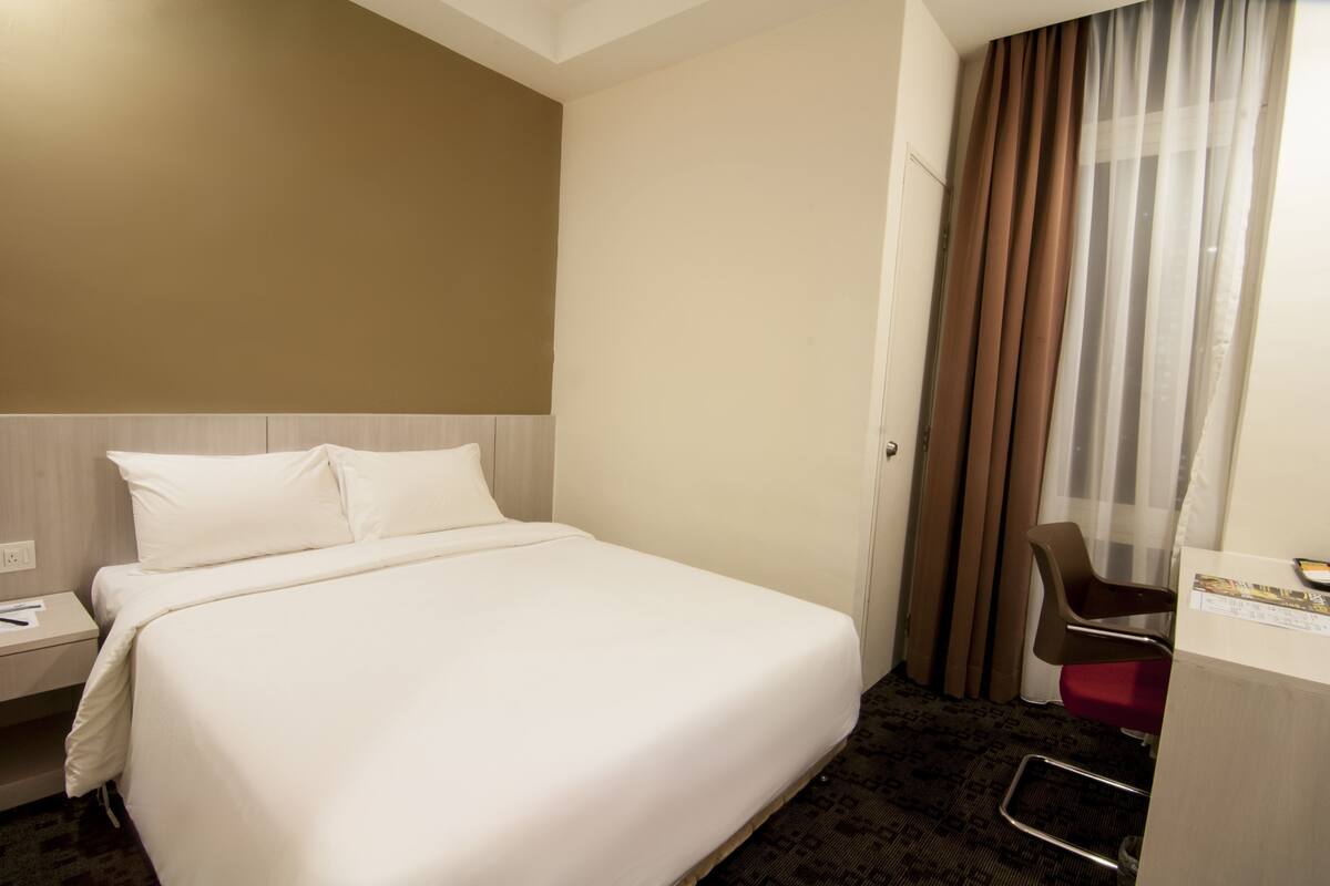 A hotel room with a bed, a desk, a chair, and a window with curtains.