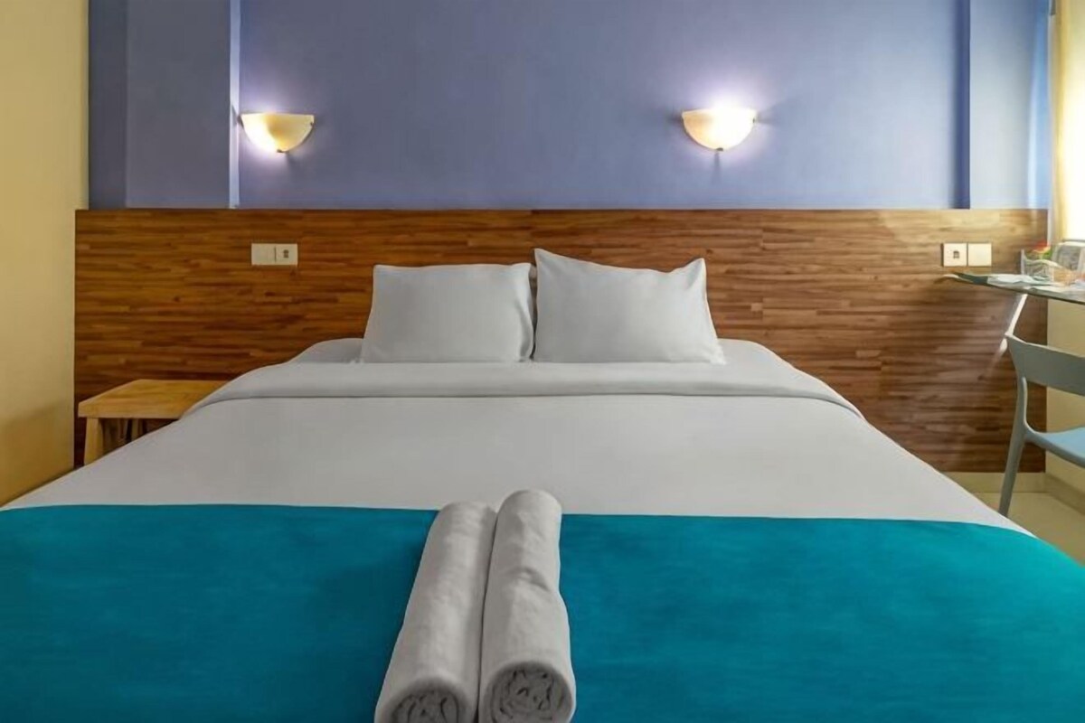 Habitació d'hotel amb un panell de fusta al capçal, dos coixins blancs, un llençol de llit color aquamarina i dos tovalloles enrotllades al llit.