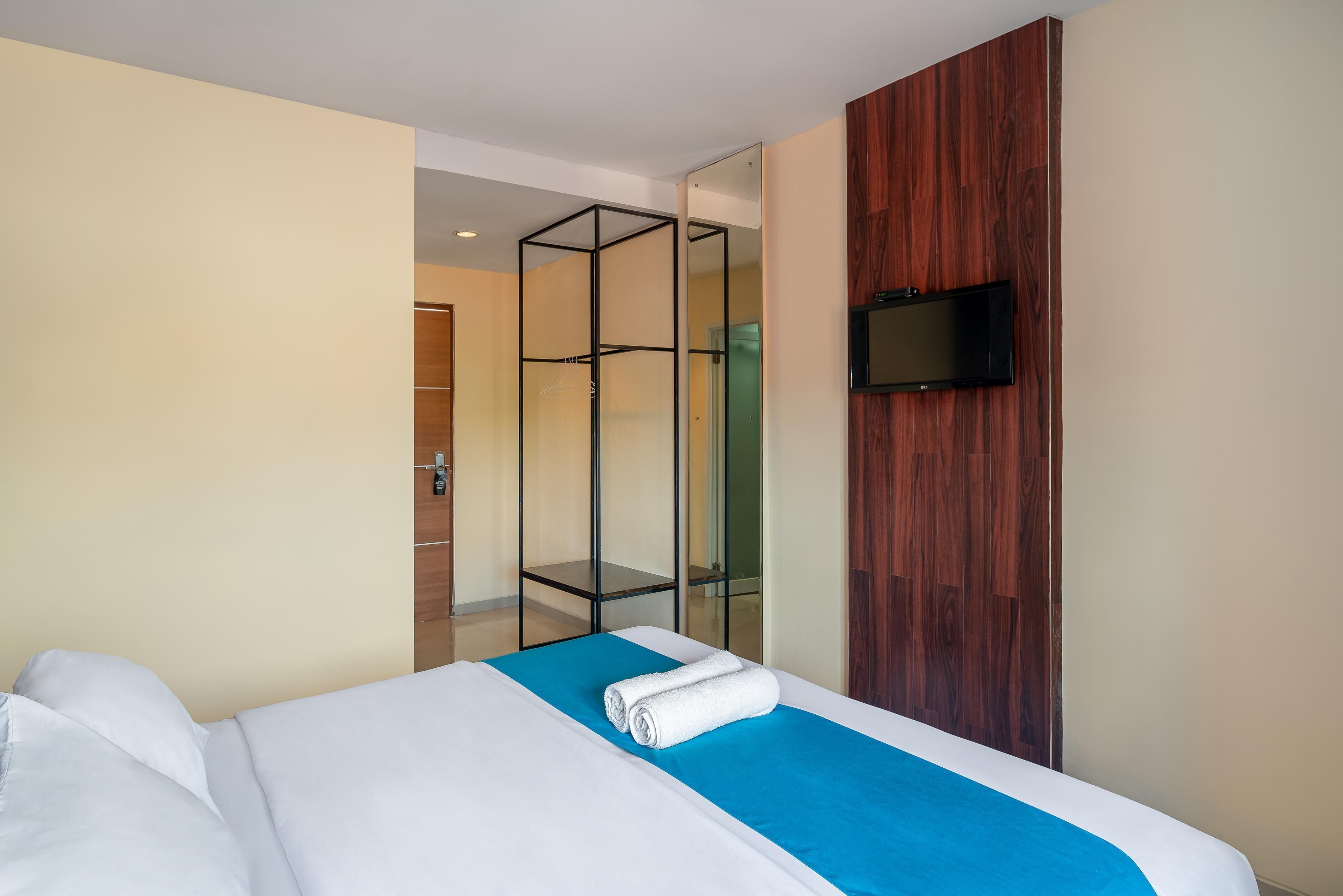 Habitación de hotel con cama, pared de acento azul, panel de madera y televisor montado en el panel.