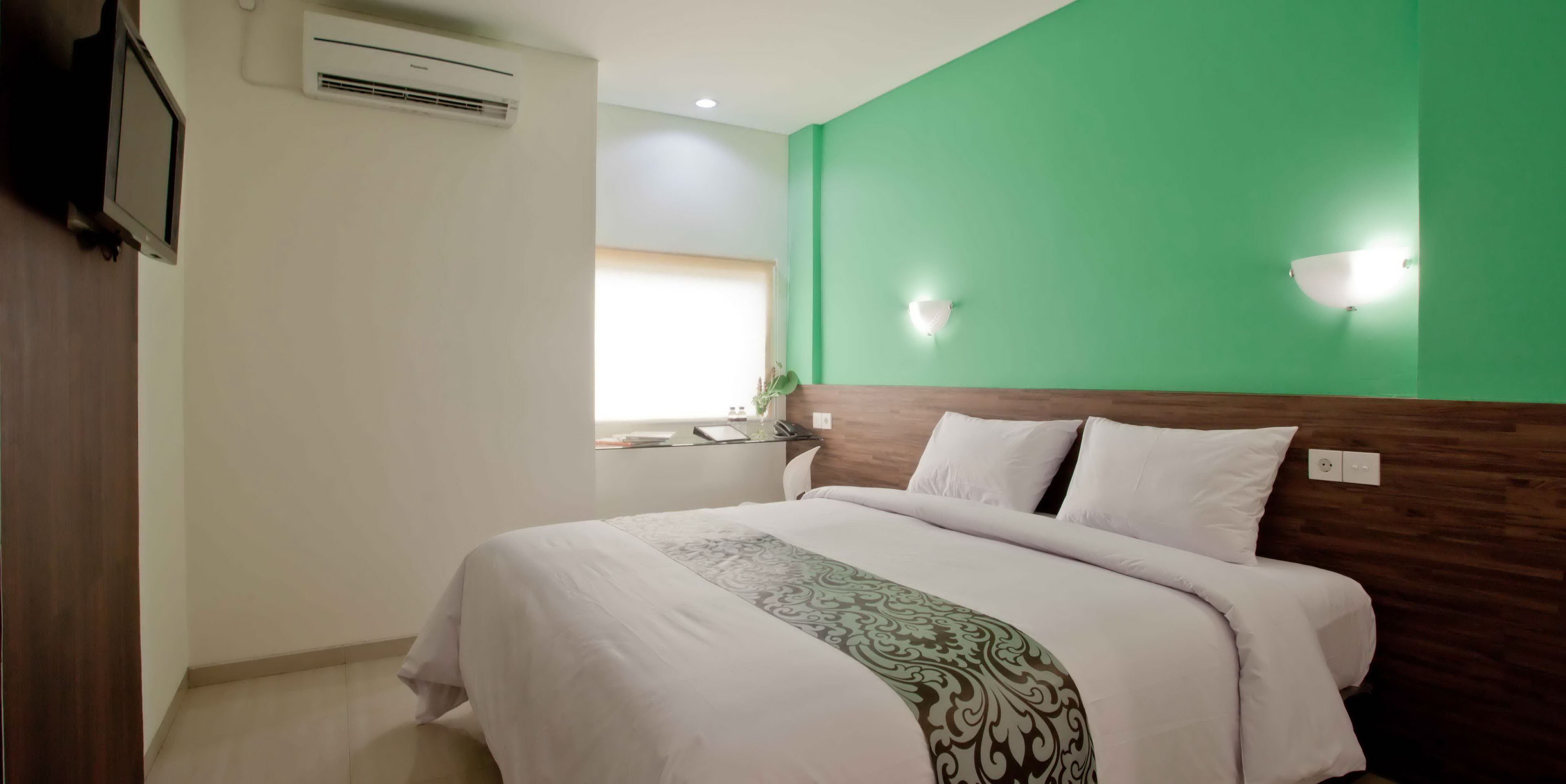 A hotel room with a bed, a green wall, a window, and an air conditioning unit.