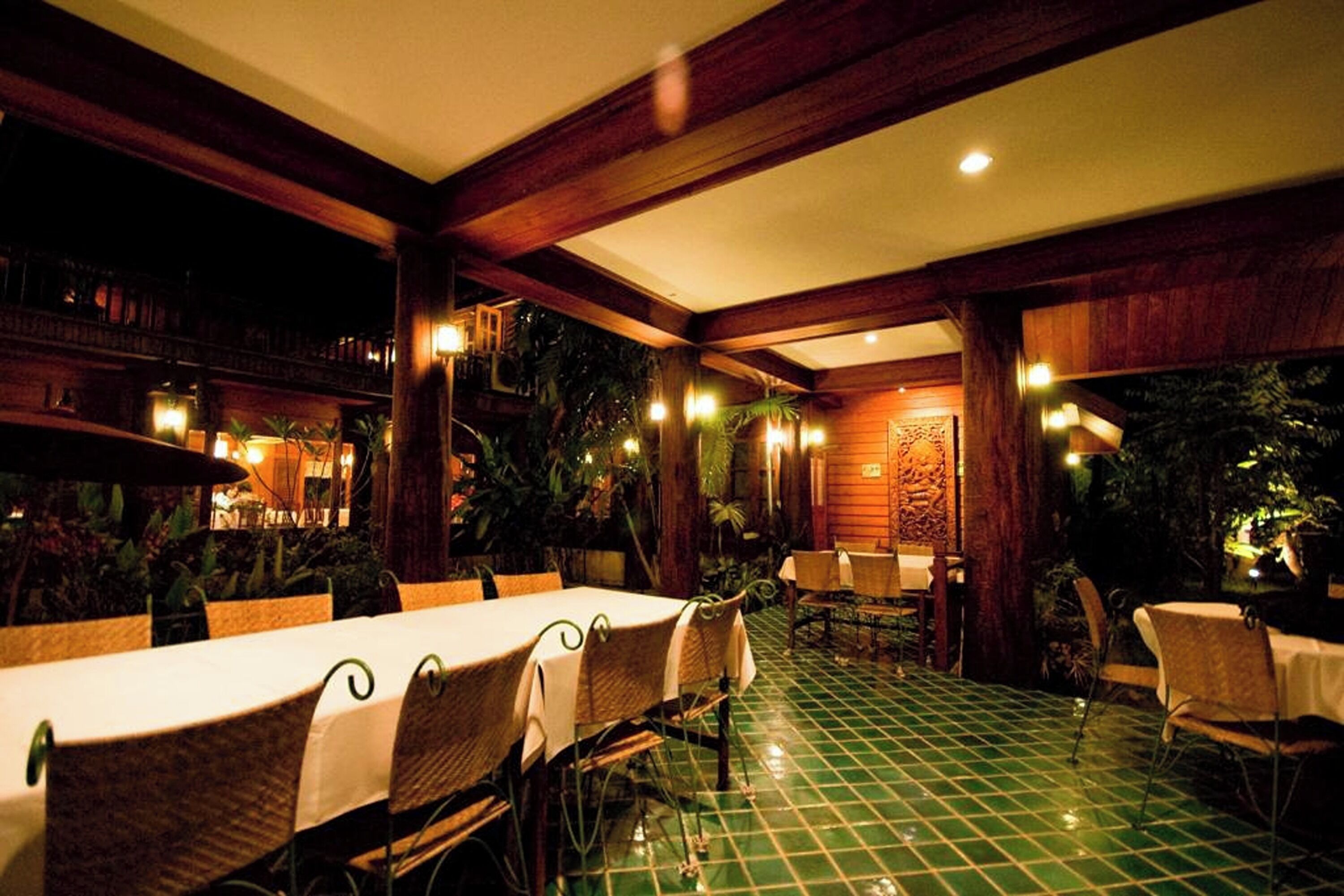 An outdoor dining area with tables and chairs, surrounded by wooden structures and greenery.