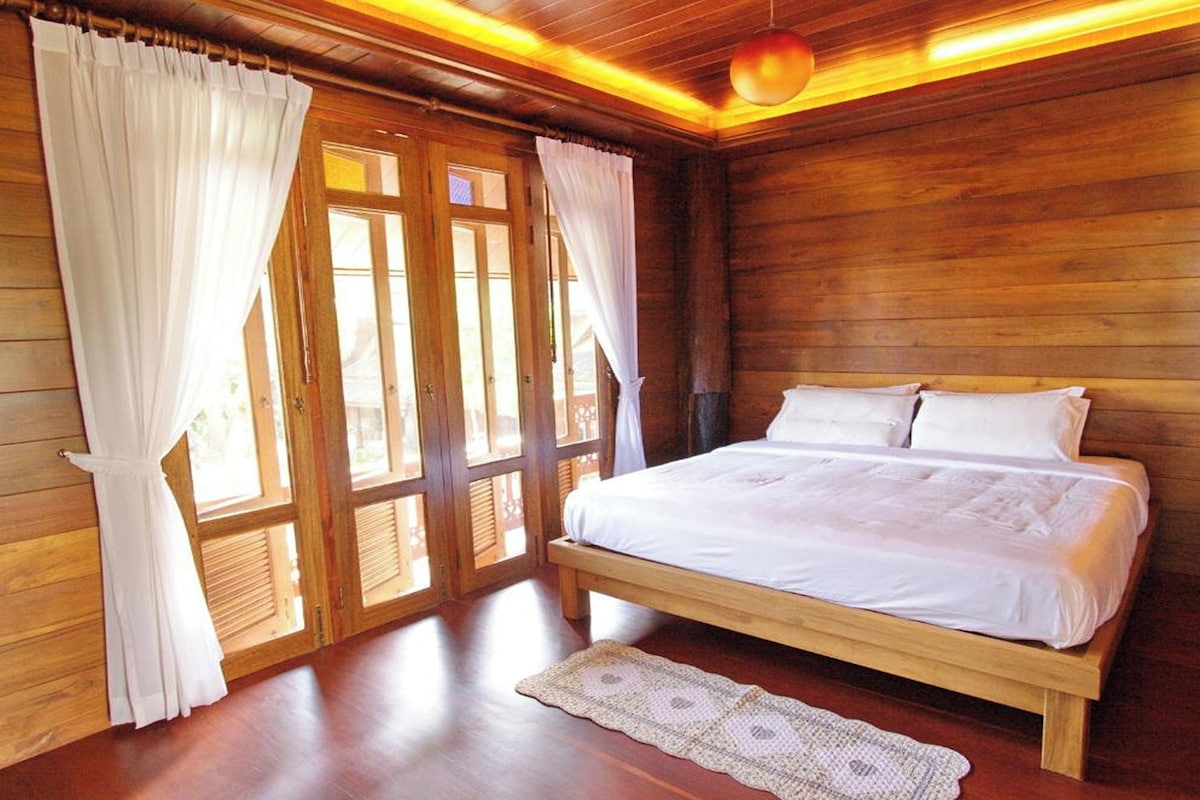 A wooden room with a bed, curtains, and a window.