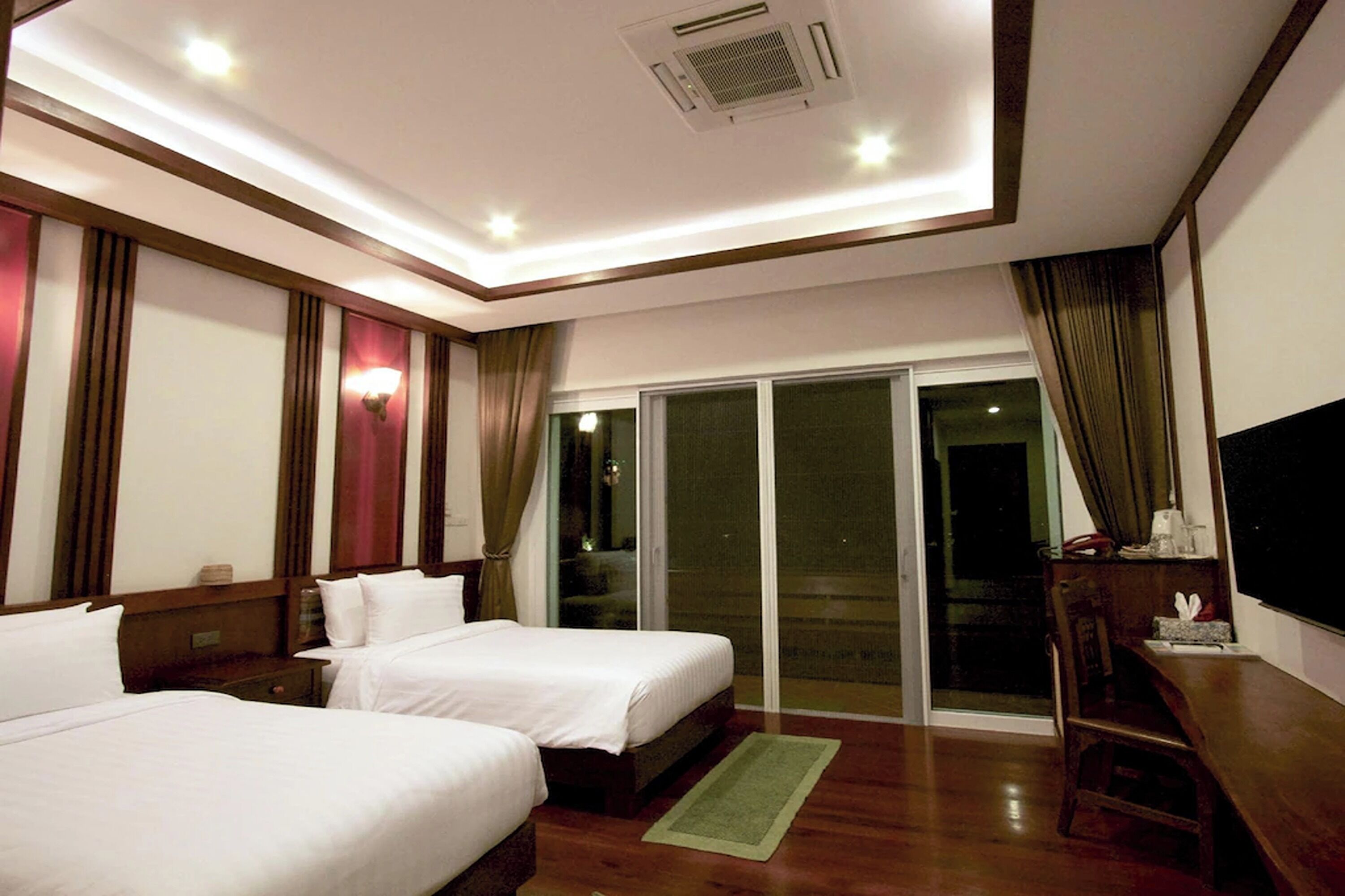 A hotel room with two beds, a desk, a chair, a TV, and a sliding glass door to the outside.