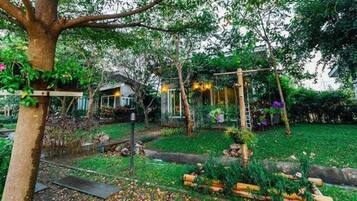 A garden with a swing set, a small house, and a tree.