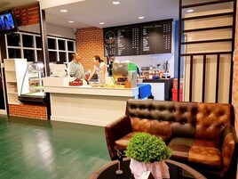 Un restaurante con mostrador, tablero de menú y zona de estar con sofá de cuero marrón y una pequeña planta verde.