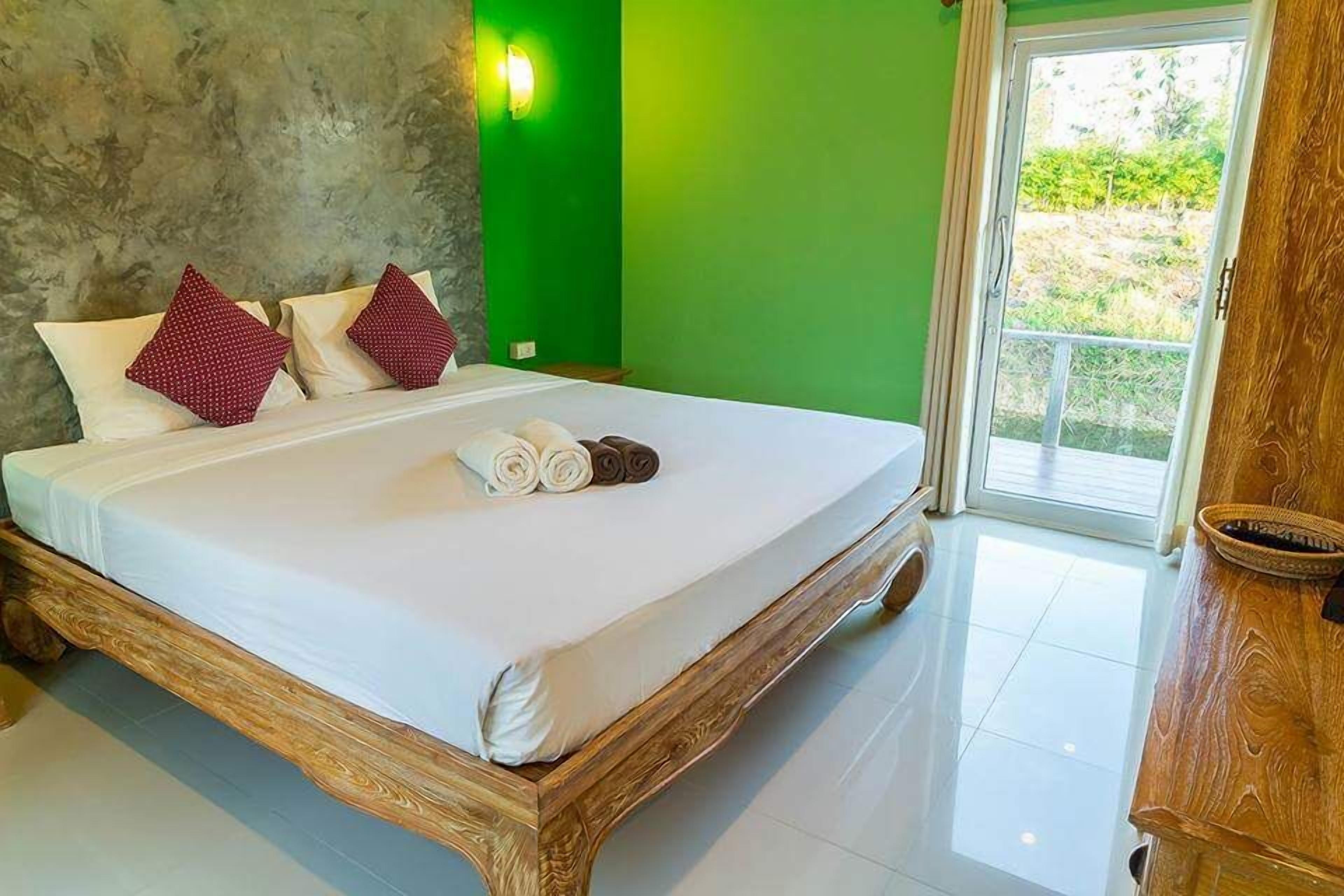 A bed with white linens, red and white pillows, and rolled towels.