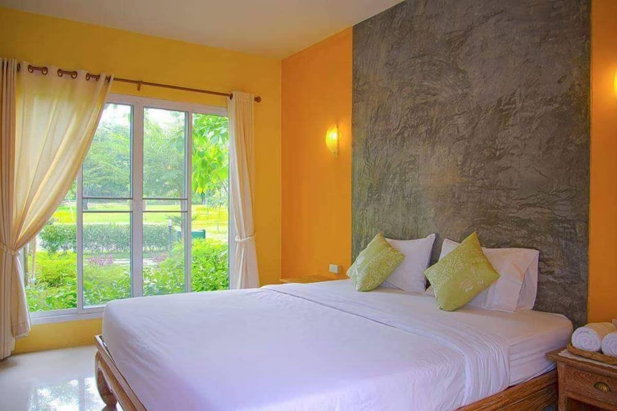Ein Schlafzimmer mit einem großen Bett, Blick ins Grüne durch das Fenster und einer Wand mit Steinoptik.