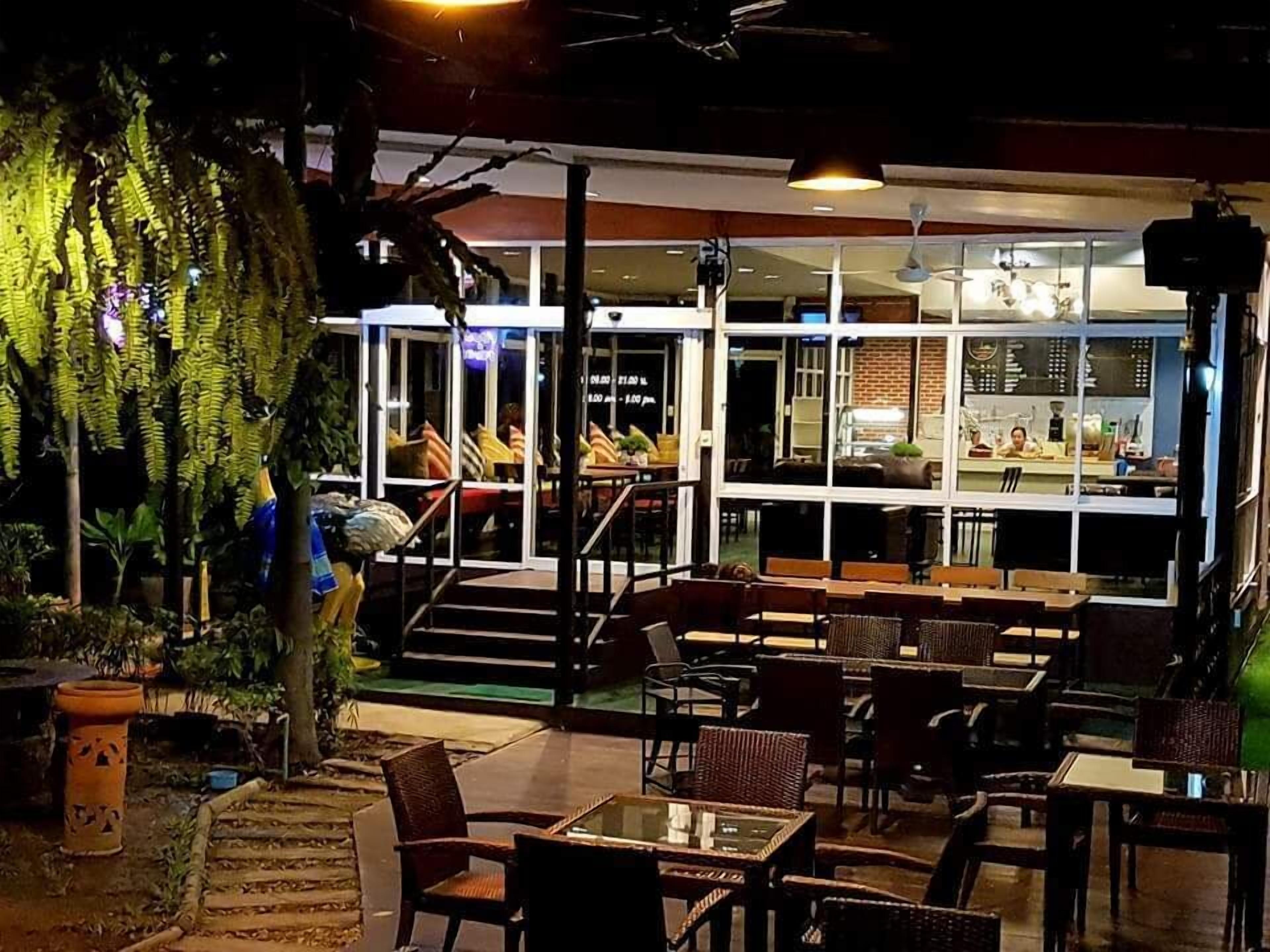 An outdoor seating area with tables and chairs, a staircase leading to an indoor area, and a large plant to the left.