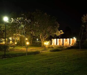 Spazio esterno notturno con sentieri illuminati e un edificio con diverse stanze.