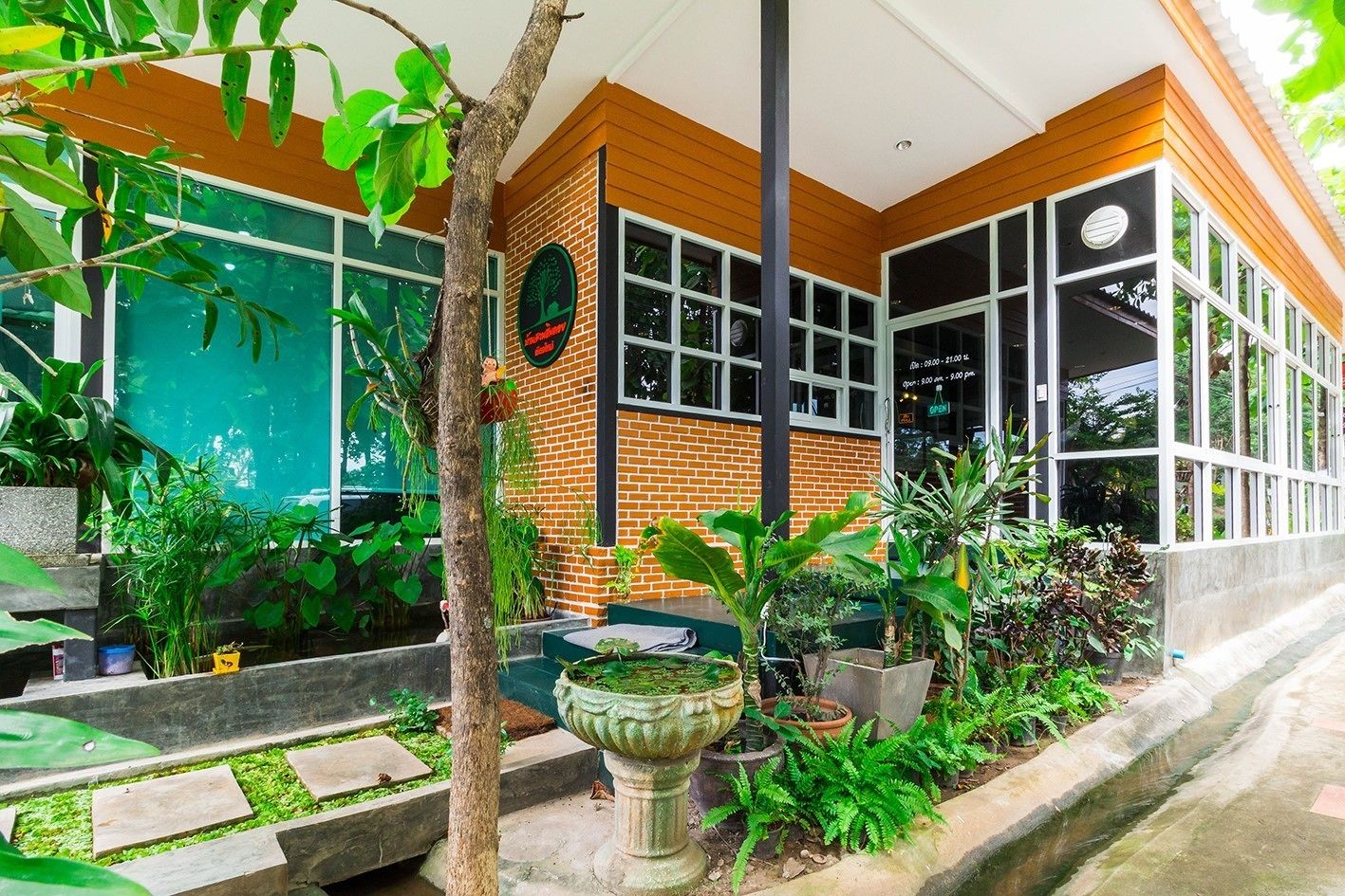 A modern building with a brick facade, large windows, and a well-maintained garden with various plants and a decorative fountain.