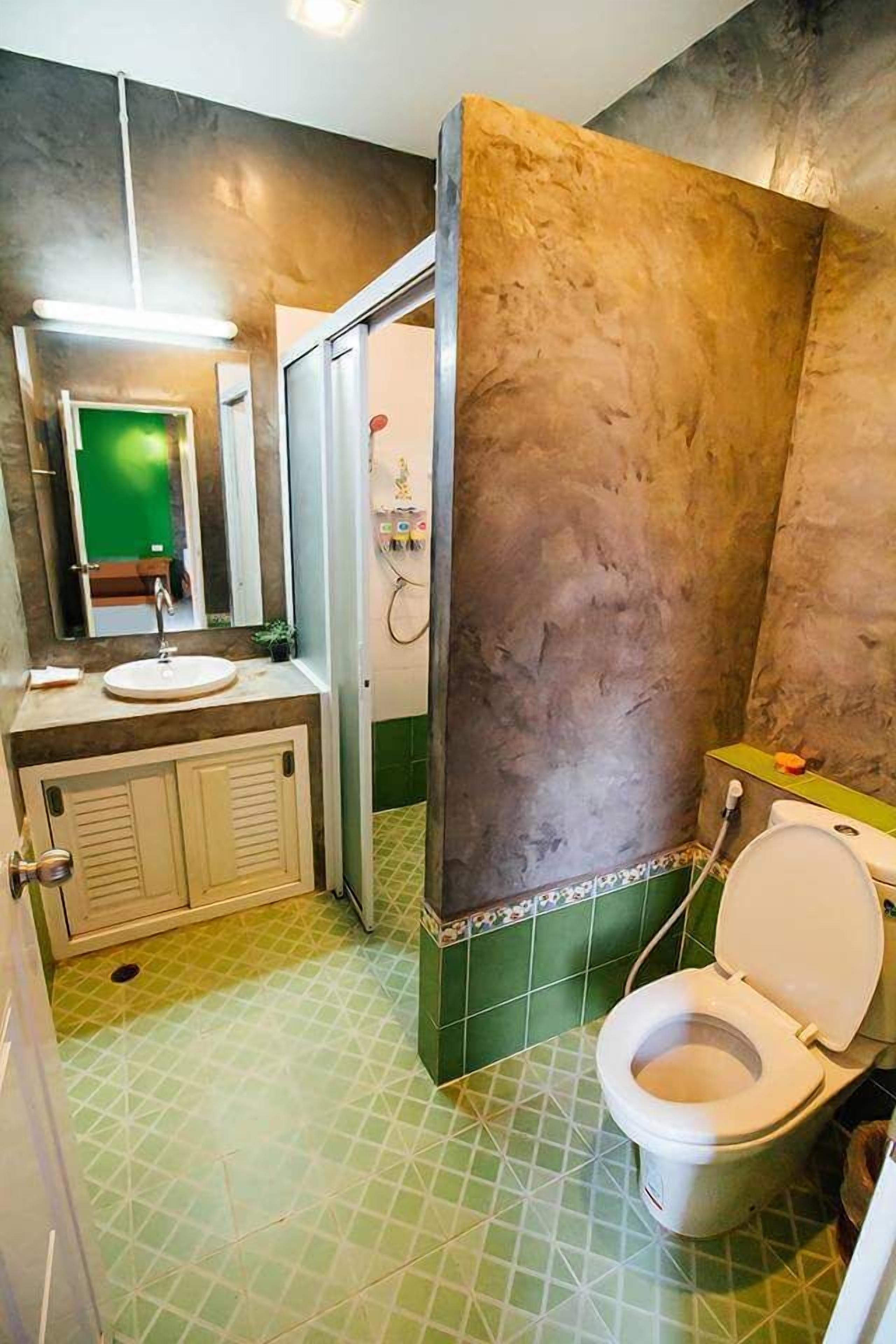 A bathroom with a green tiled floor, a white sink, a mirror, and a shower area.