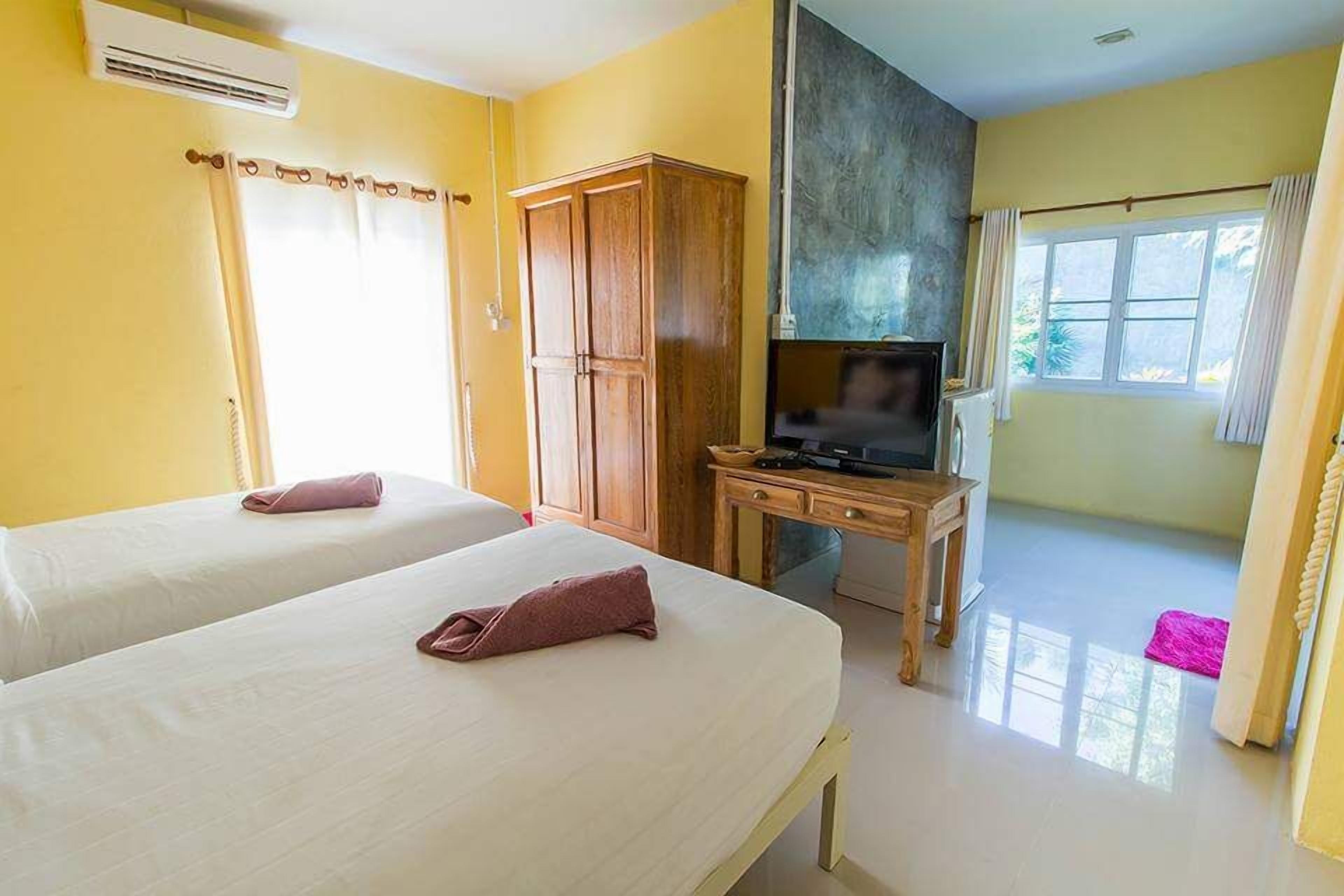 Habitación de hotel con dos camas, un armario de madera, un televisor sobre una mesa de madera y una ventana con cortinas.