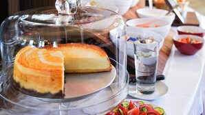 A buffet table with a cheesecake, a plate of sliced tomatoes, and various bowls of food.