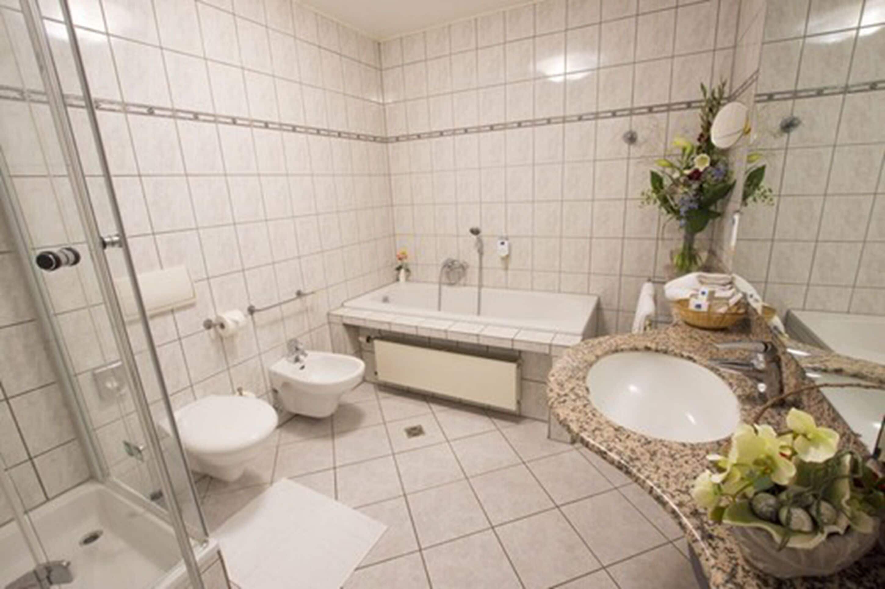 A modern bathroom with a glass shower enclosure, a toilet, a bidet, a bathtub, and a vanity with a sink and mirror.