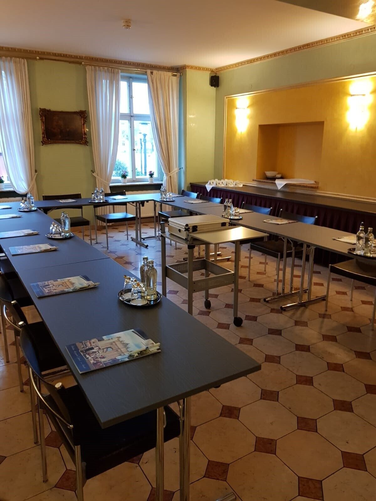 Un salón de conferencias con mesas largas, sillas y un gran ventanal con cortinas.