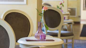 A dining area with a table set for two, featuring a vase with a single rose and a candle.