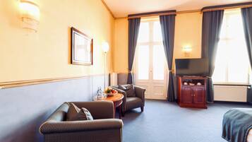 Ein Hotelzimmer mit Sofa, Sessel, Fernseher und einem kleinen Tisch mit Obstschale.